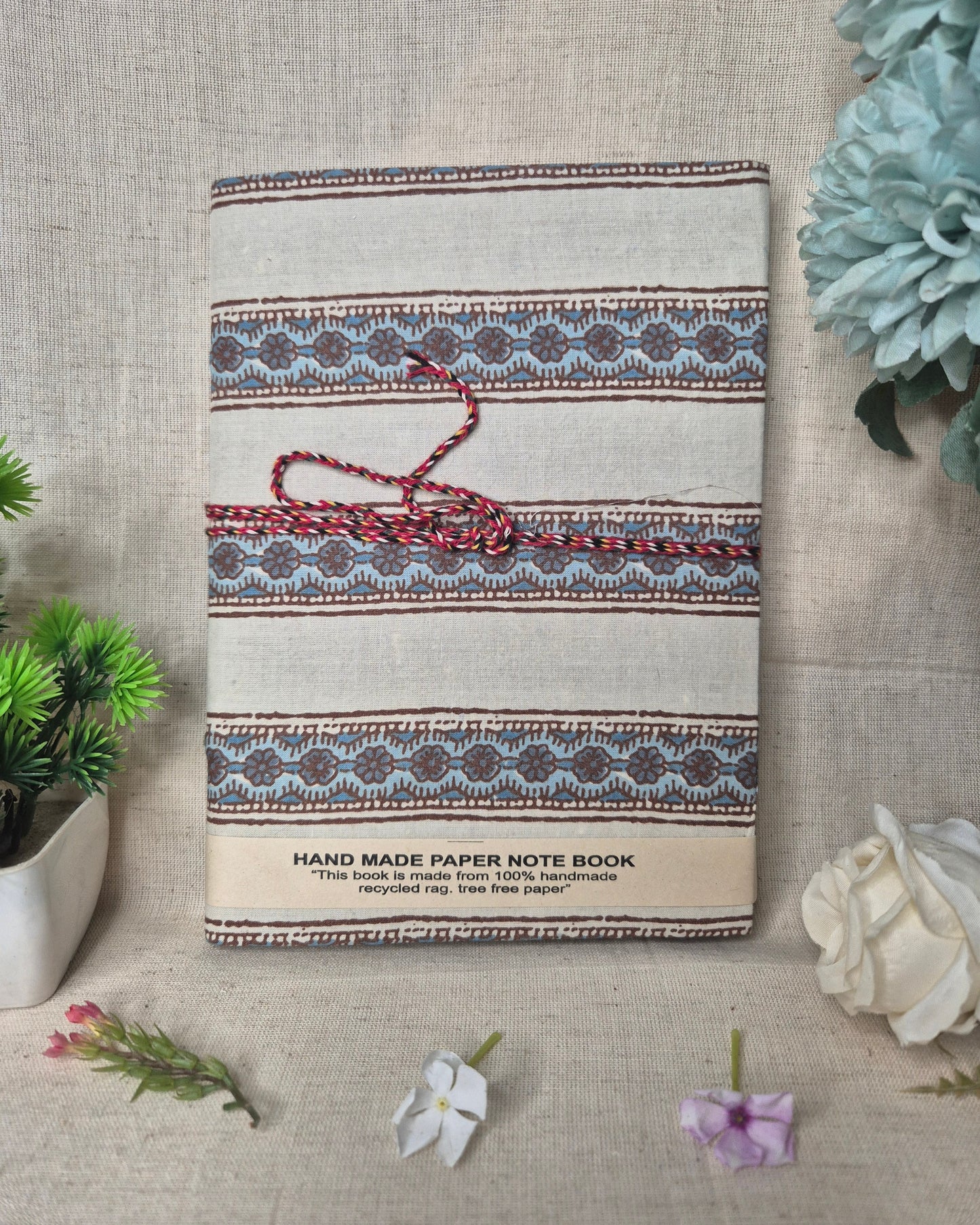 Handmade paper notebook with decorative cover on a textured surface with plants.