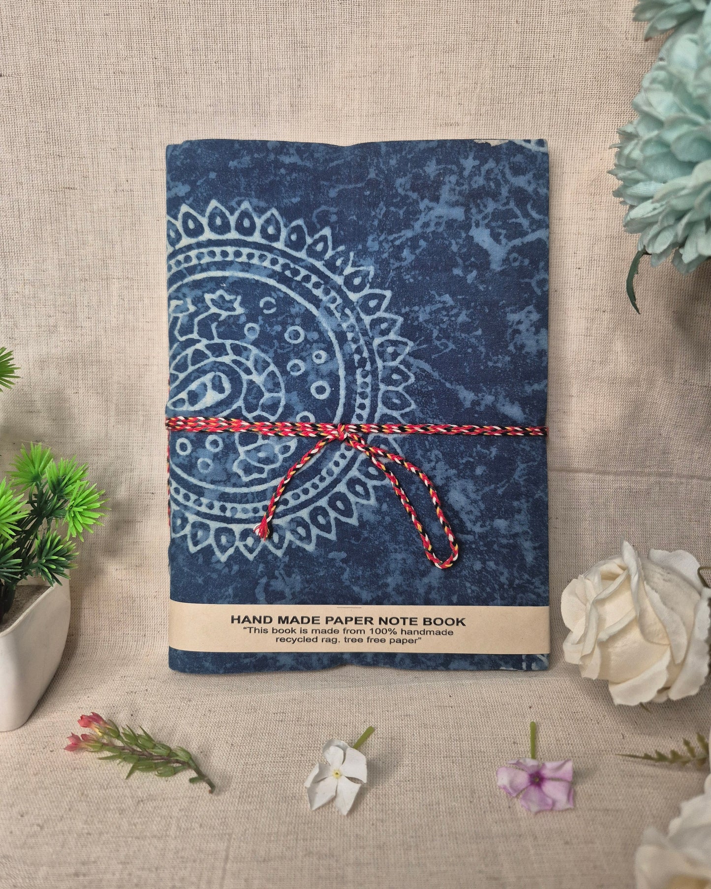 Blue notebook with a decorative pattern and red string on a beige surface with flowers.