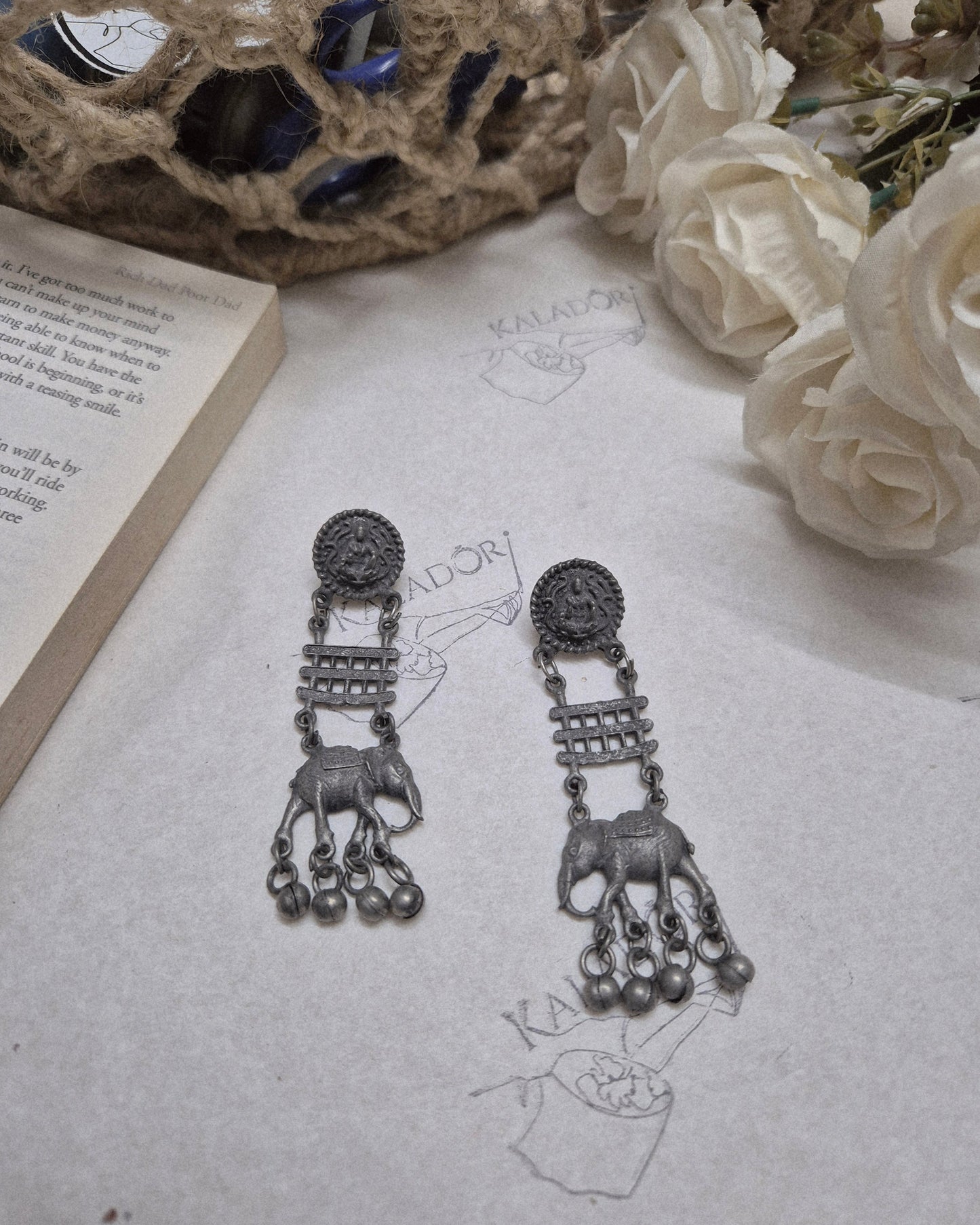 Pair of ornate earrings on a textured surface with flowers and an open book.