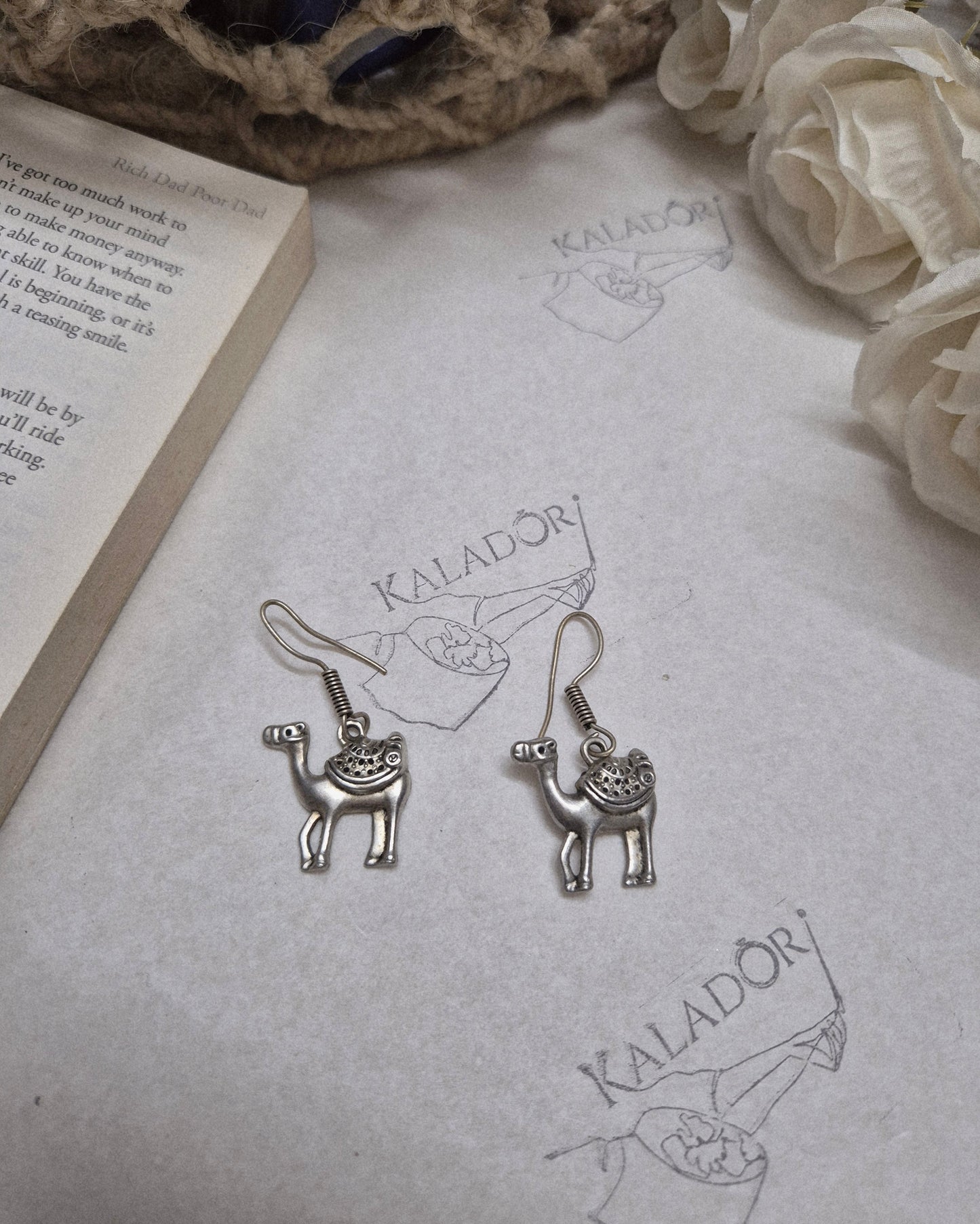 Silver animal-shaped earrings on a textured surface with floral and text elements.