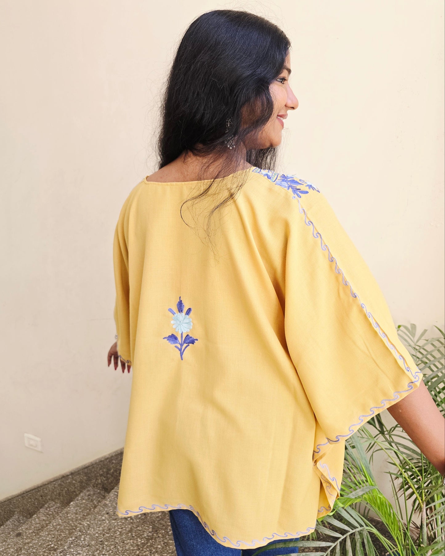 Person wearing a yellow outfit with floral embroidery on a neutral background