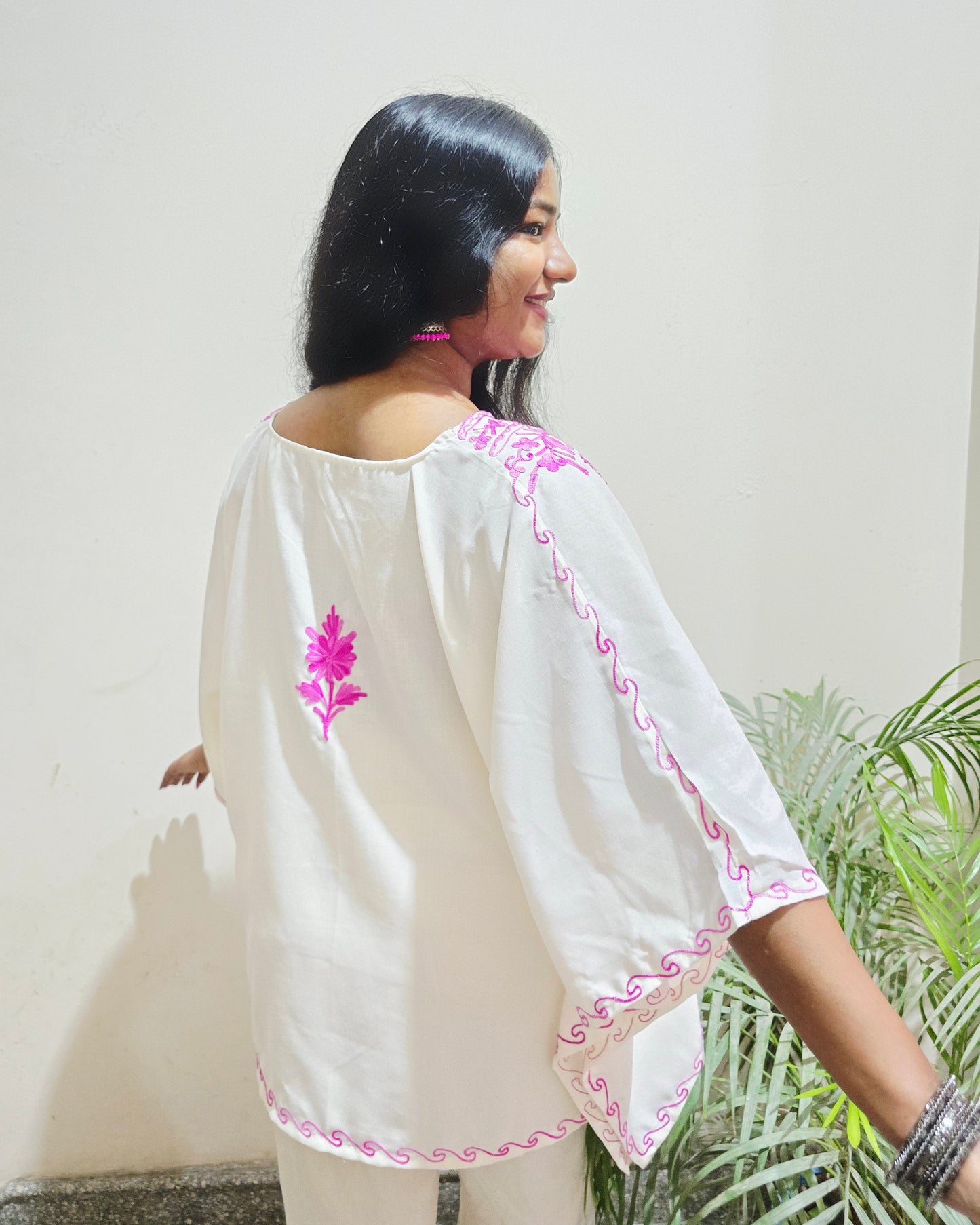 Person wearing a white outfit with pink embroidery on a light background