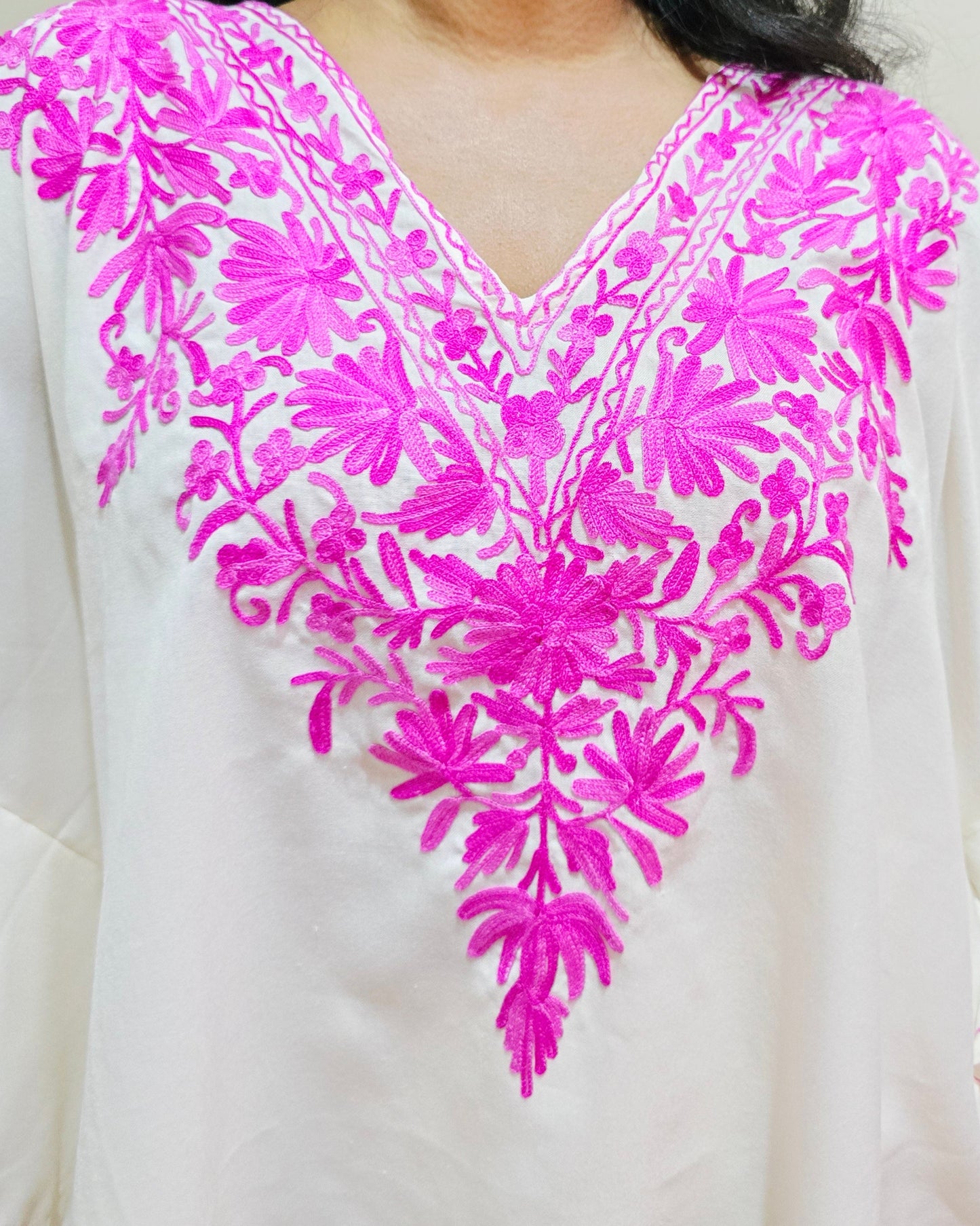 White garment with pink floral embroidery on a plain background