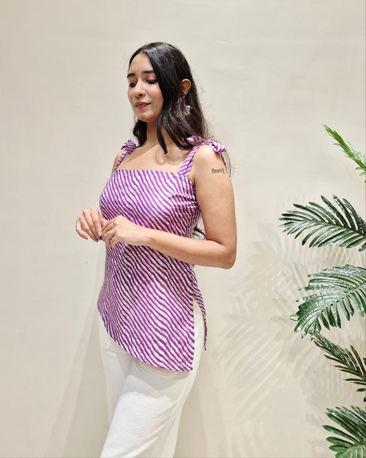 Woman wearing a purple striped short kurti and white pants against a beige background with green leaves.