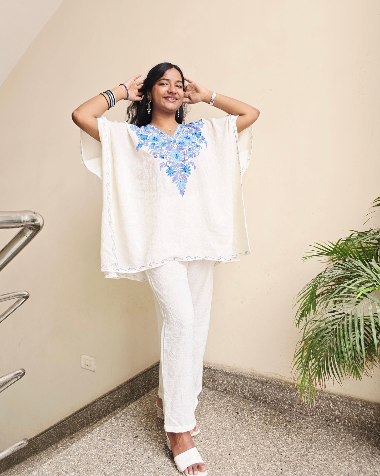 Woman in a white outfit with floral design standing indoors.