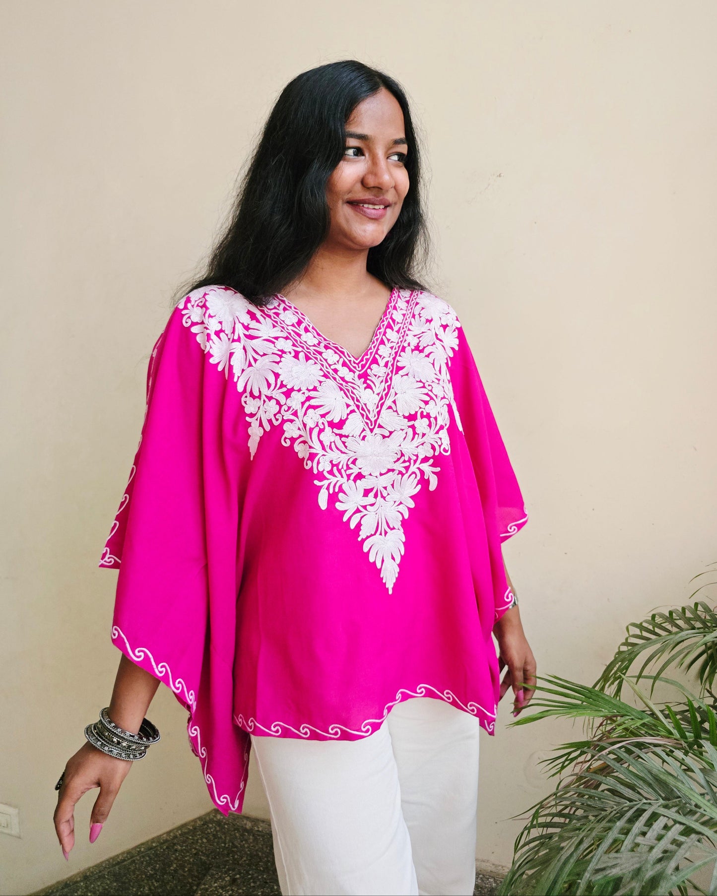 Woman wearing a bright pink traditional outfit with white embroidery on a beige background