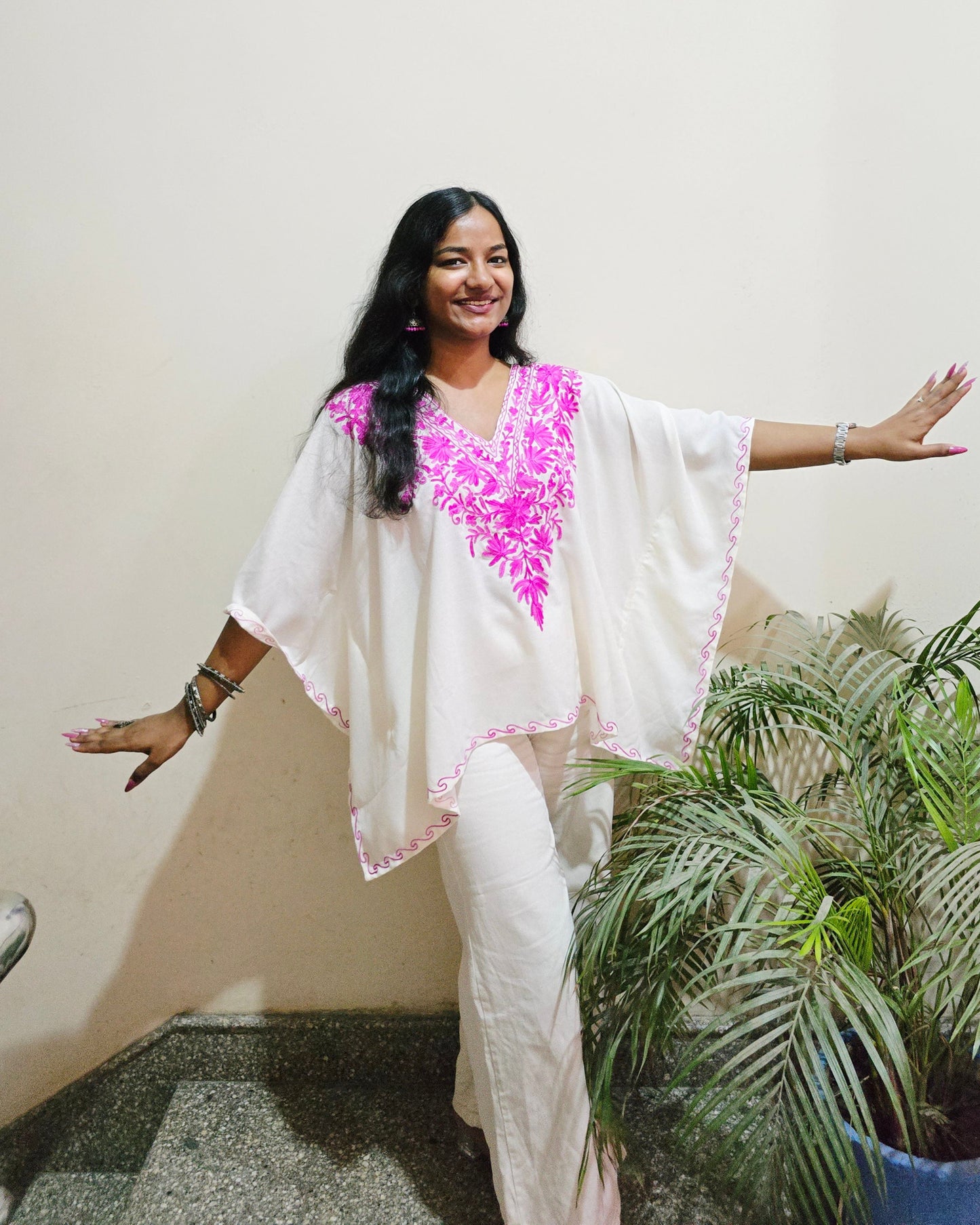 Woman in a white and pink traditional outfit standing indoors with plants in the background