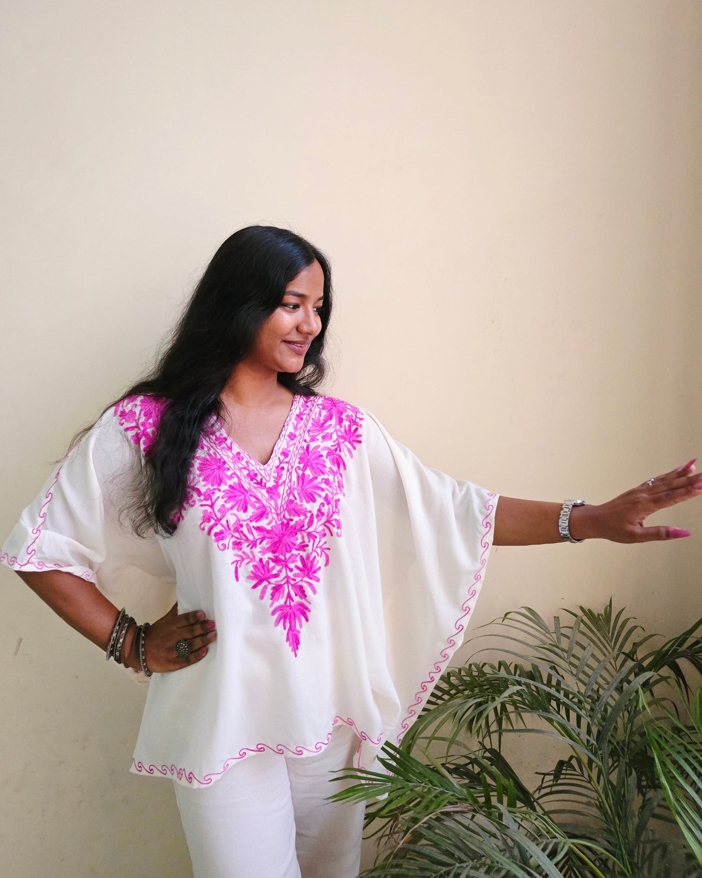Woman in a white top with pink floral patterns standing indoors.
