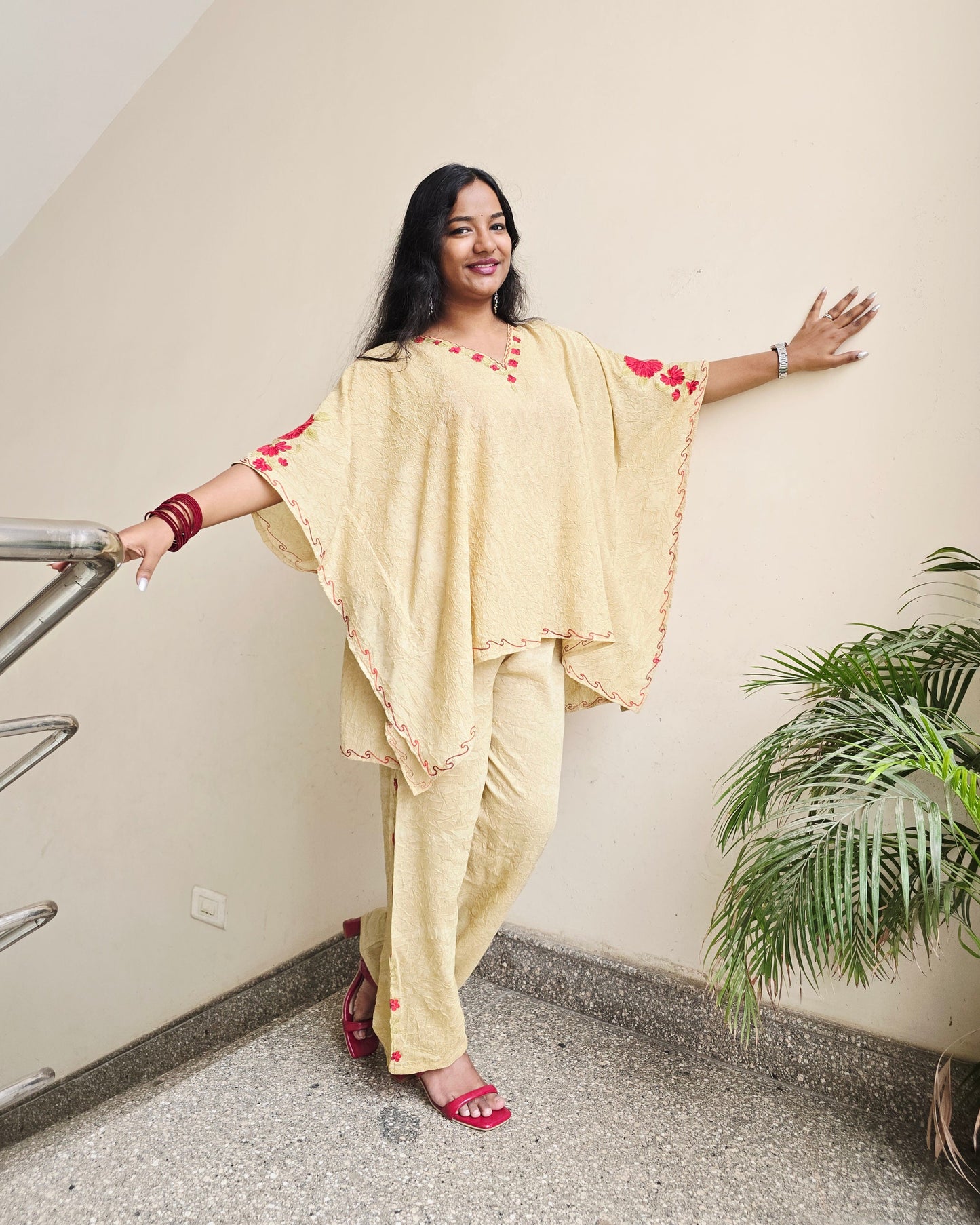 Woman in a yellow saree standing on a ladder indoors with a plant in the background