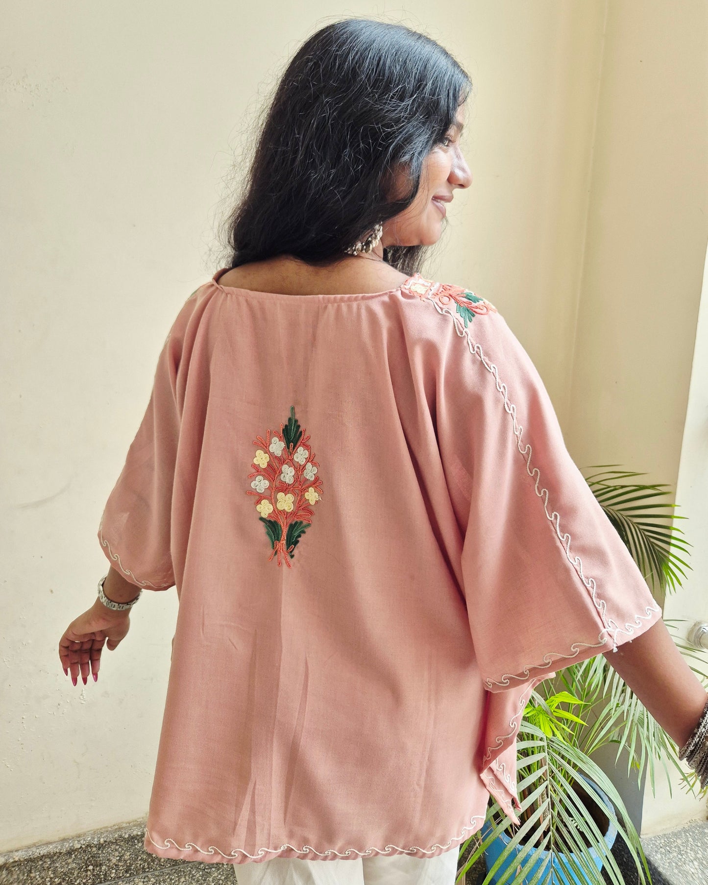 Person wearing a pink embroidered top with a neutral background