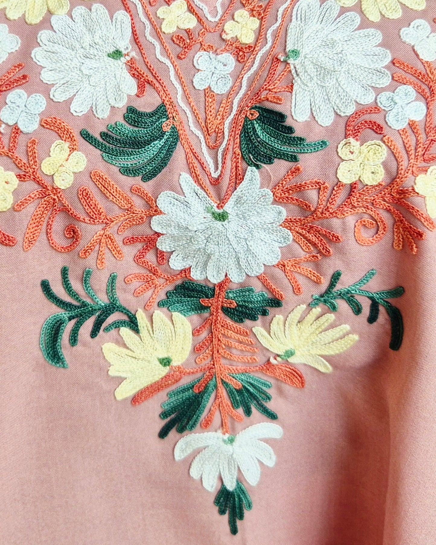 Close-up of floral embroidery on a garment with pink background