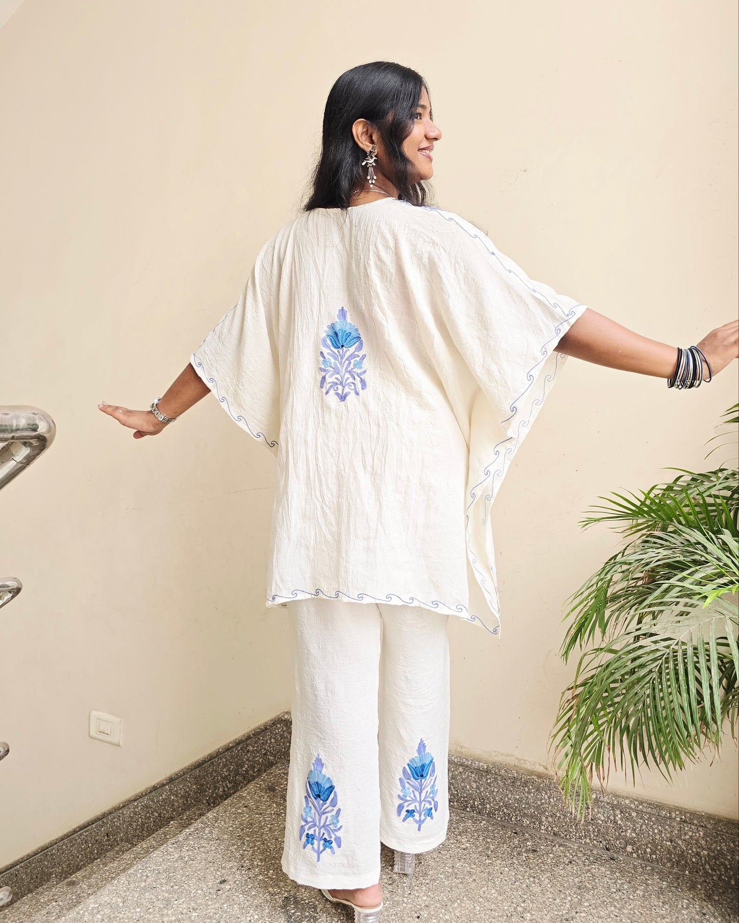 Person wearing a white outfit with blue floral patterns in an indoor setting.
