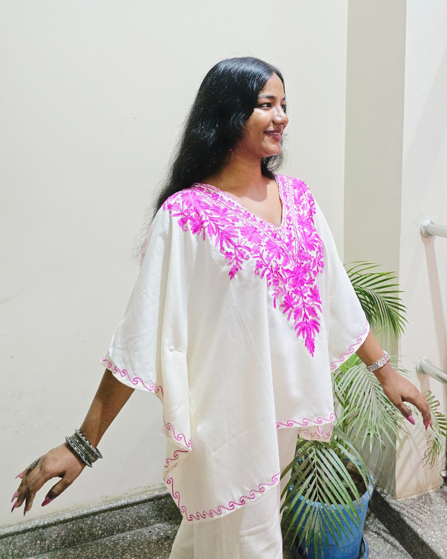 Woman wearing a white dress with pink floral embroidery in a room.