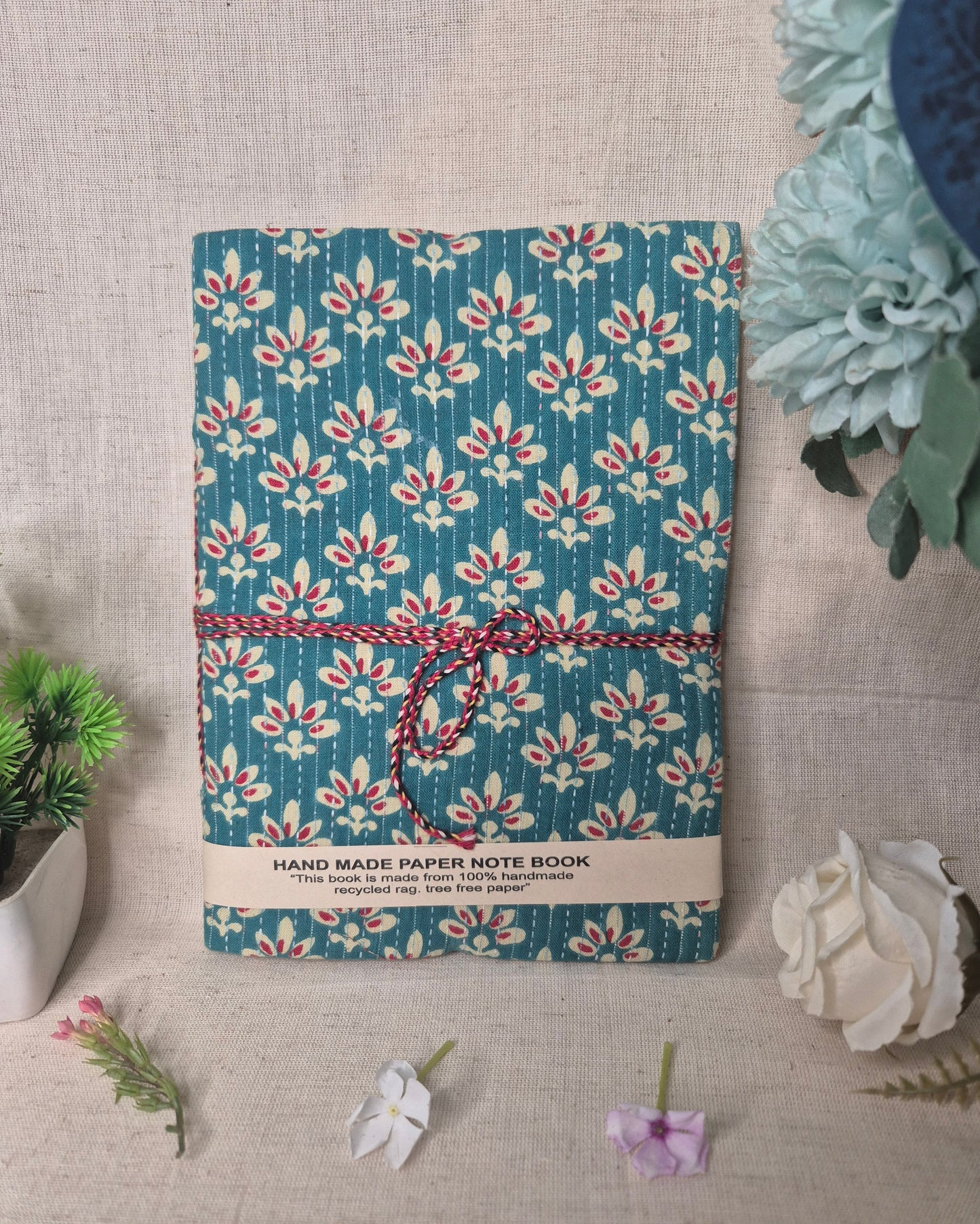 Floral-patterned notebook with a string closure on a textured surface with decorative elements.