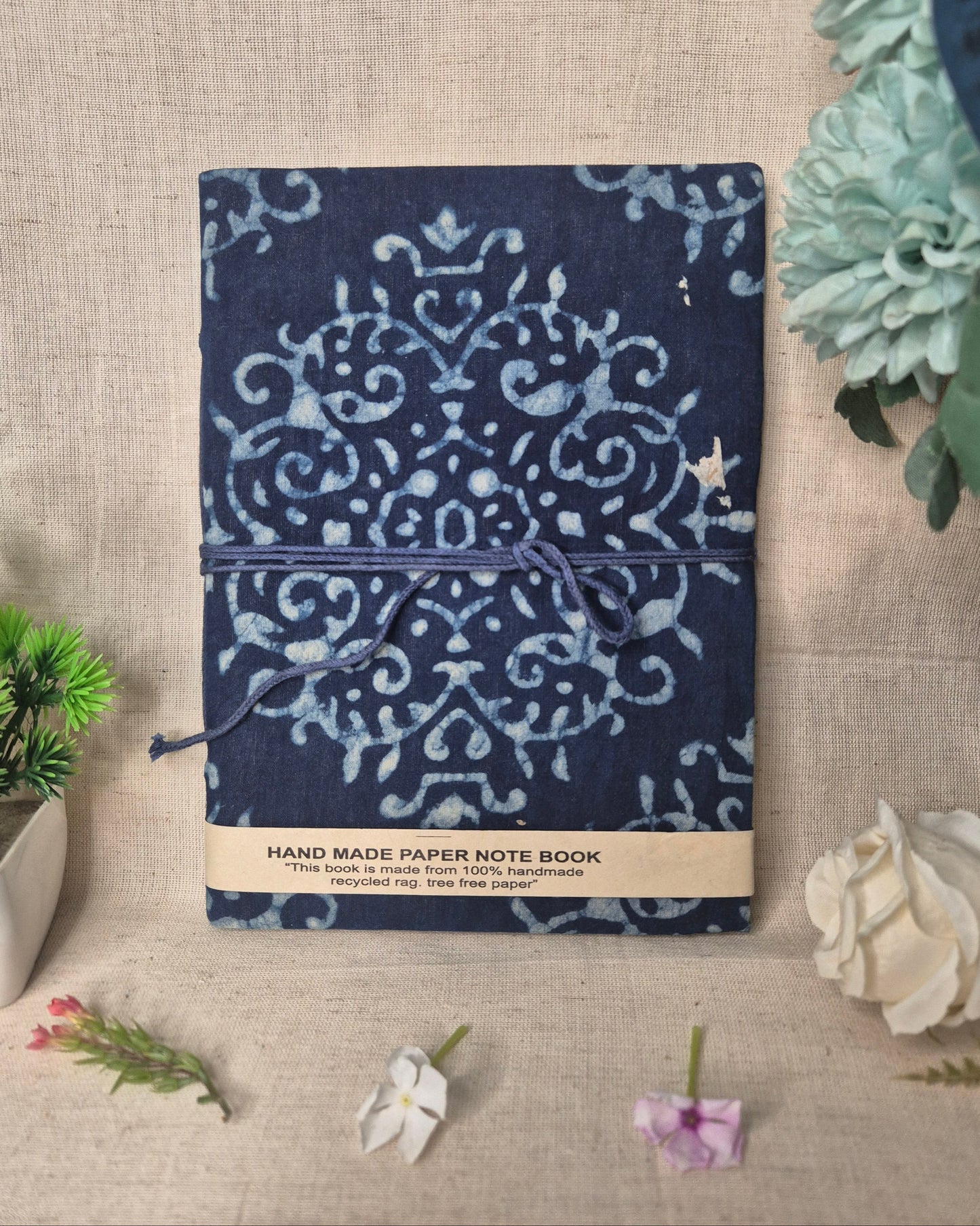 Blue patterned notebook on a textured surface with decorative plants.