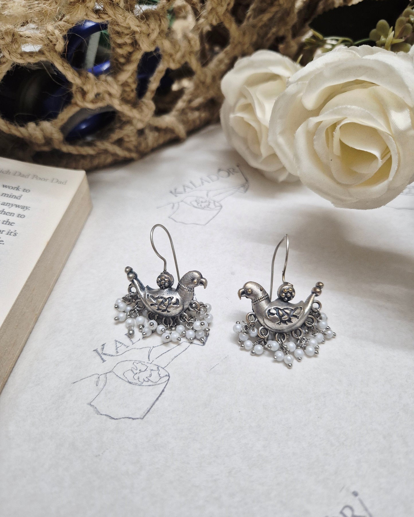 Silver earrings on a textured surface with a white rose and lace fabric.