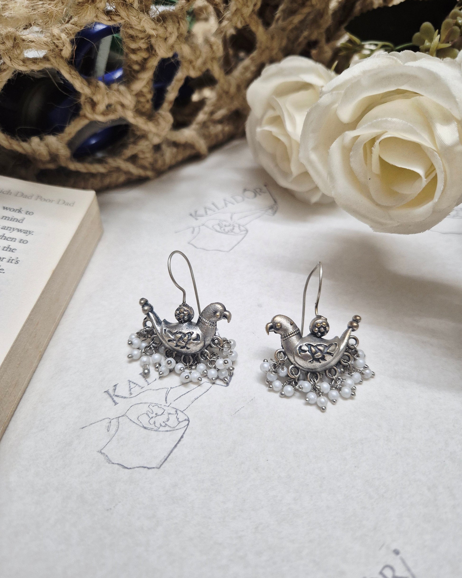 Silver earrings on a textured surface with a white rose and lace fabric.