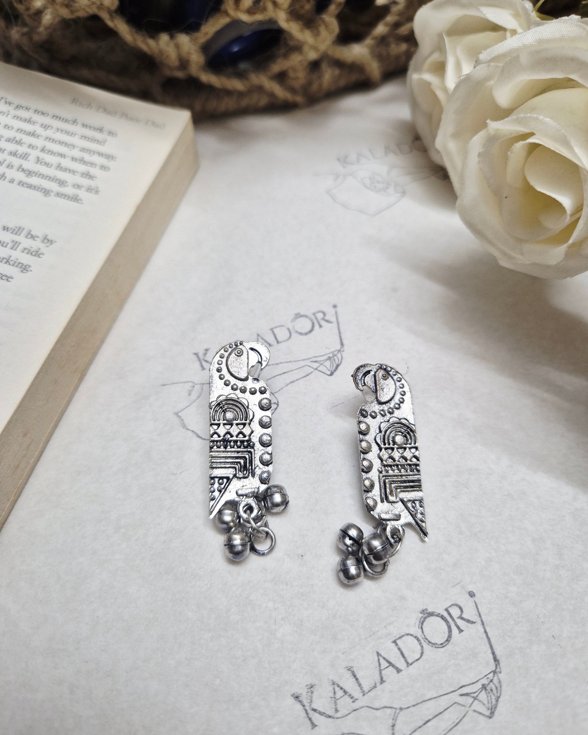 Silver earrings on a white surface with a book and decorative elements.