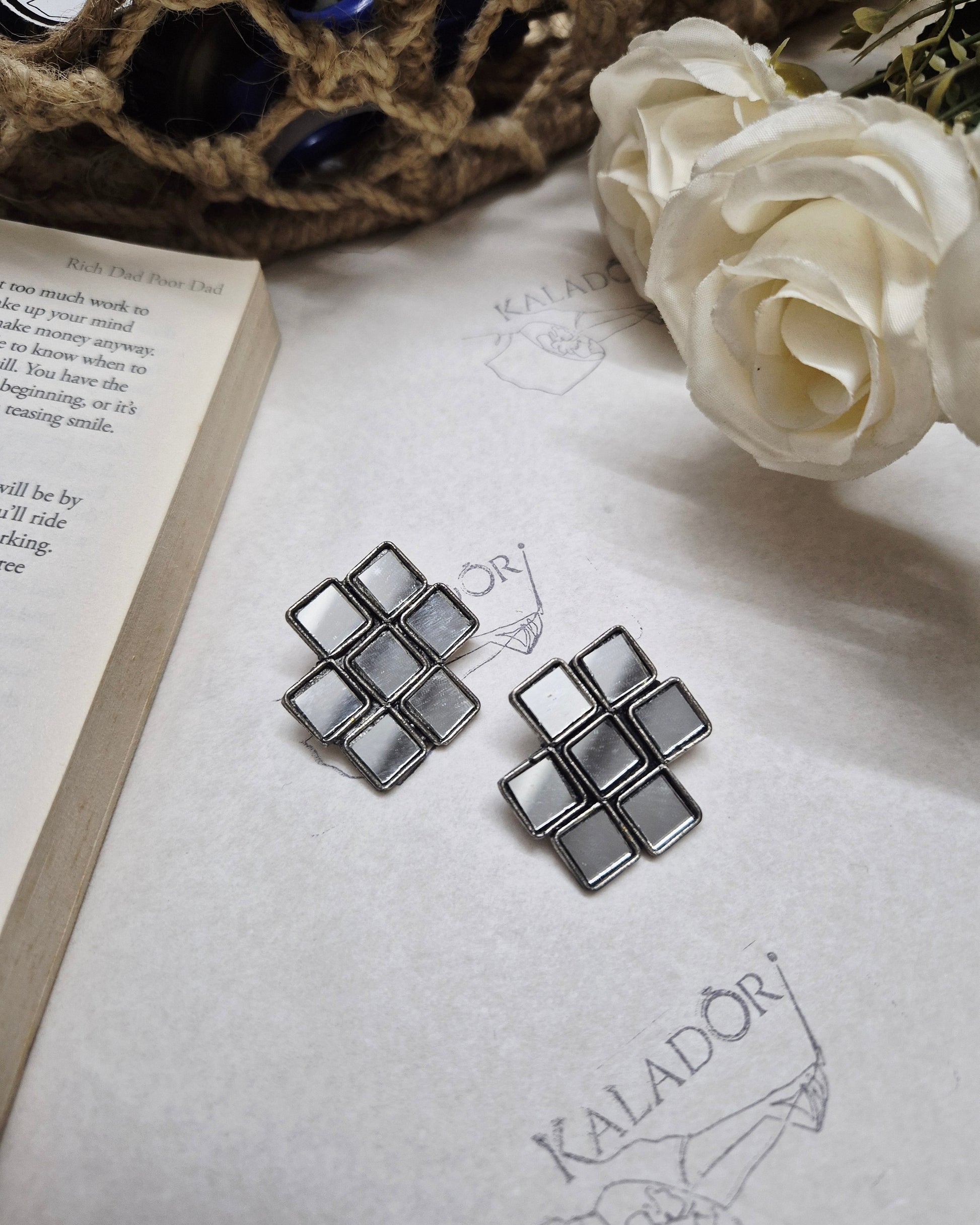 Decorative metal pieces on an open book with flowers and a woven object in the background
