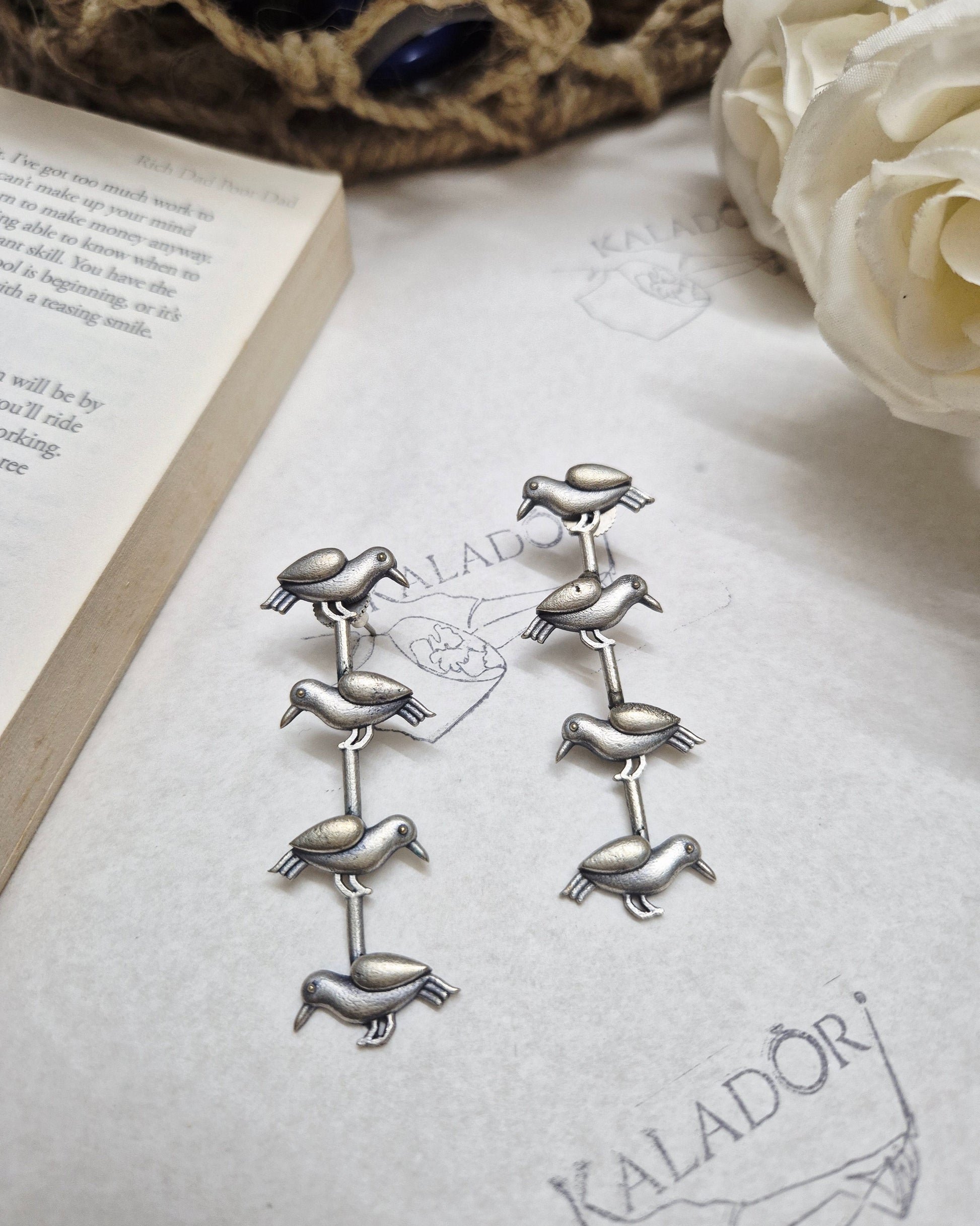 Silver animal-shaped brooches on a textured surface with a book and flowers.