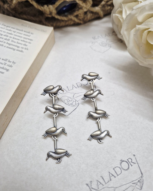 Silver animal-shaped brooches on a textured surface with a book and flowers.