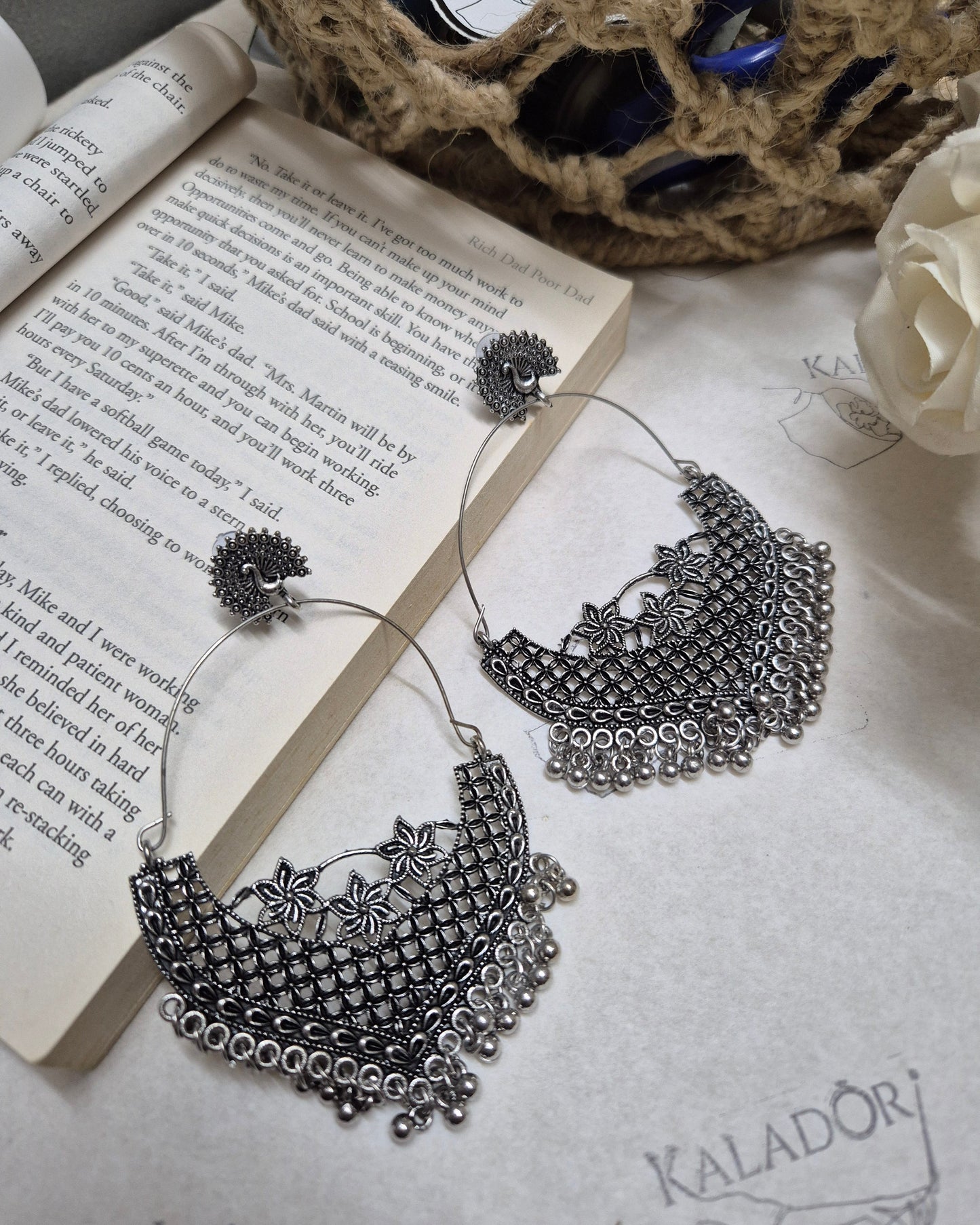 Decorative silver earrings on an open book with a white flower and textured surface.