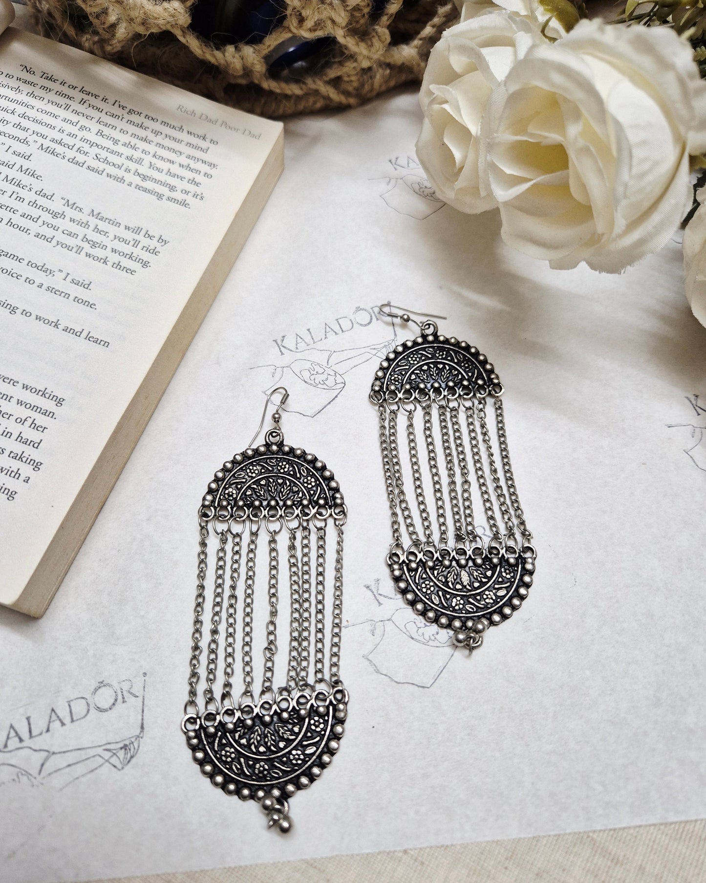 Ornate silver earrings on an open book with white roses