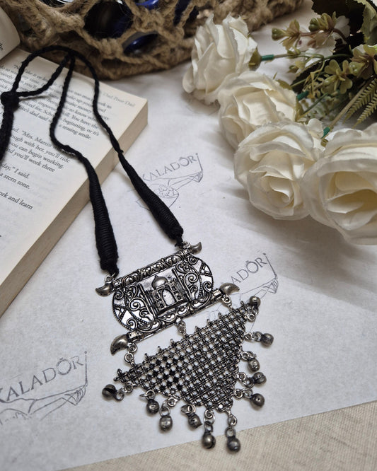 Decorative silver bookmark on an open book with white flowers and a decorative object in the background.