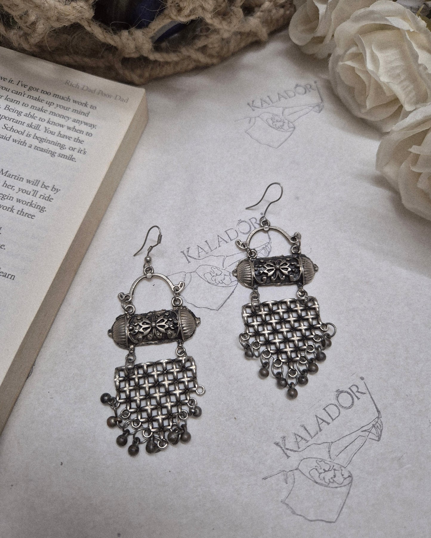 Pair of silver earrings on an open book with floral and decorative elements.