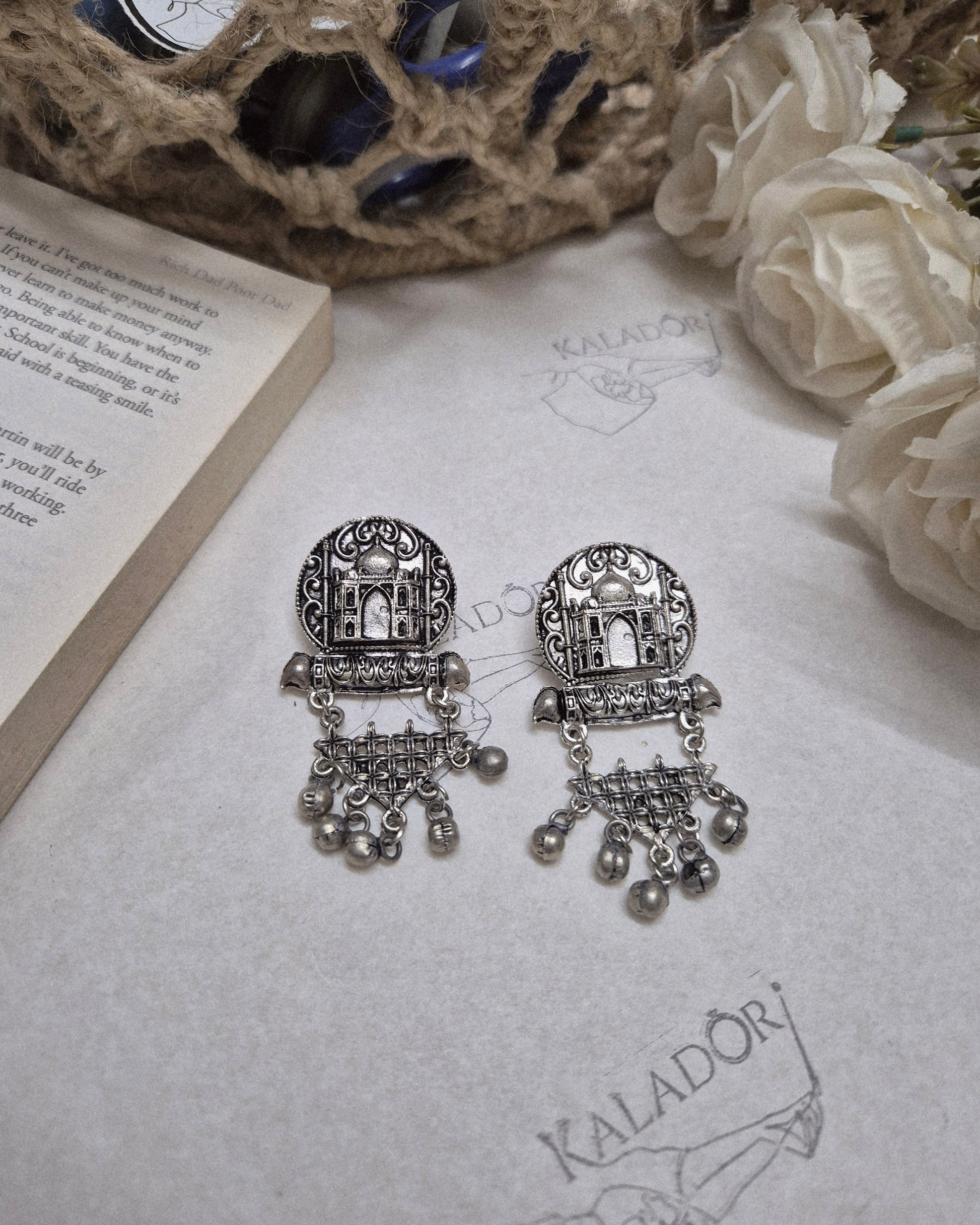 Decorative silver earrings on an open book with flowers and rope