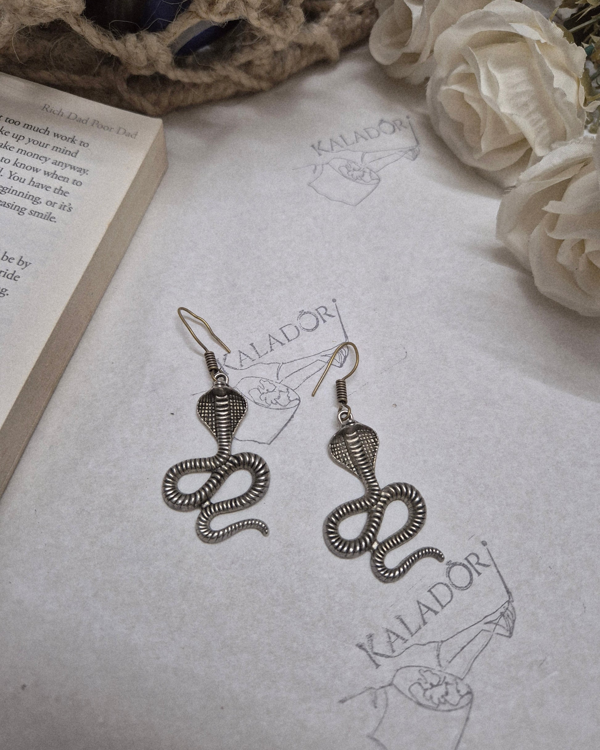 Snake-shaped earrings on a textured surface with floral and decorative elements.
