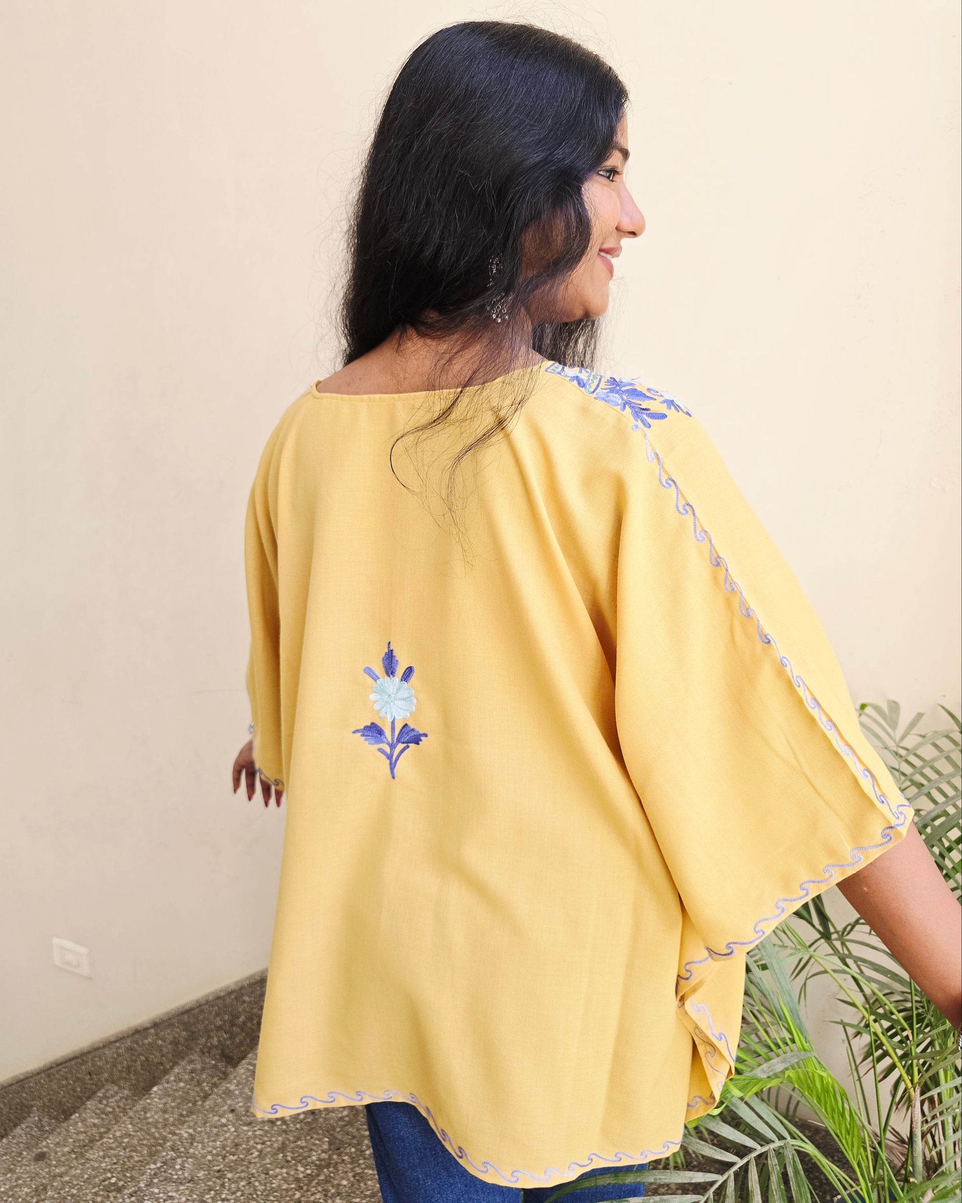 Person wearing a yellow outfit with floral embroidery on a neutral background