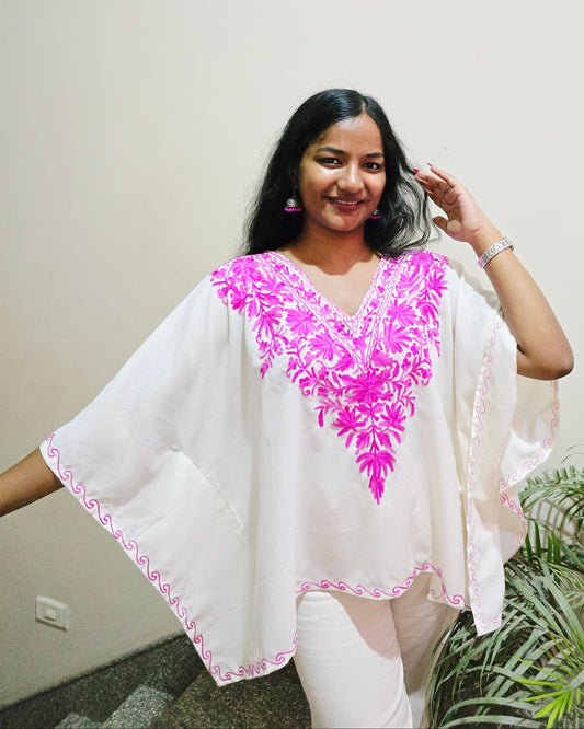 Woman wearing a white outfit with pink floral embroidery against a plain background