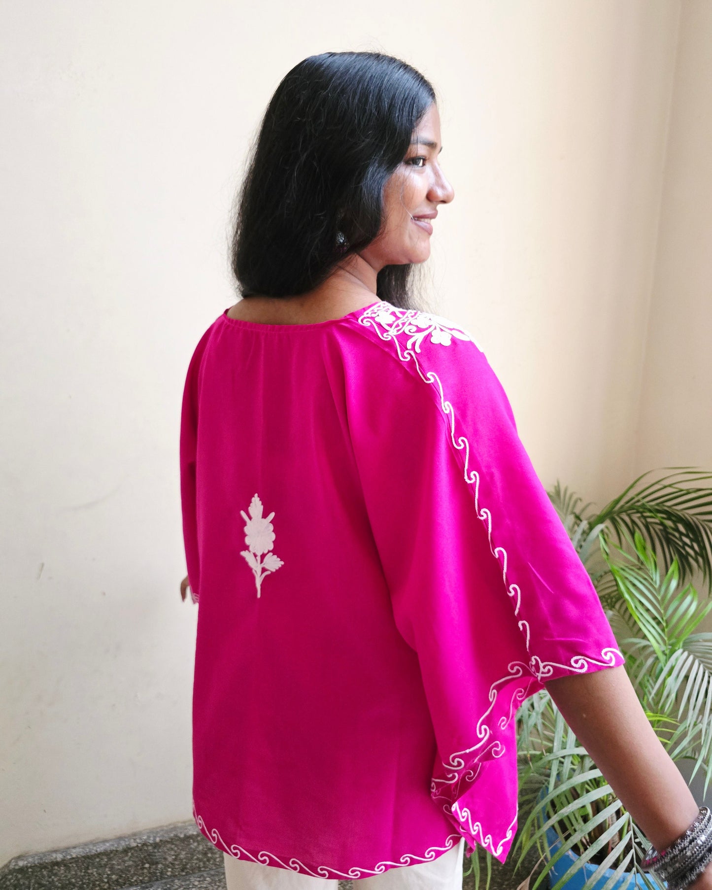 Woman wearing a pink traditional outfit with white embroidery on a light background