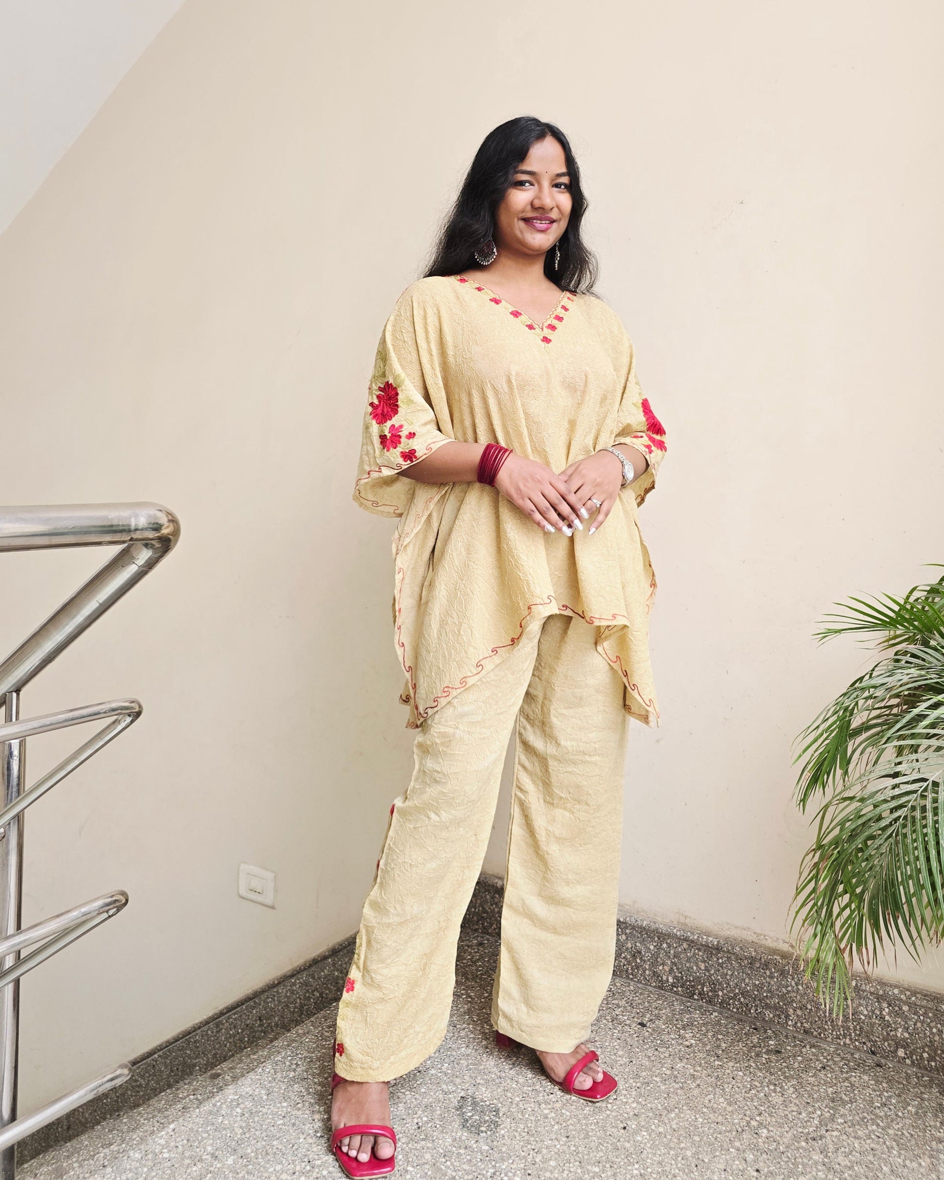 Woman in a yellow outfit with red patterns standing indoors.