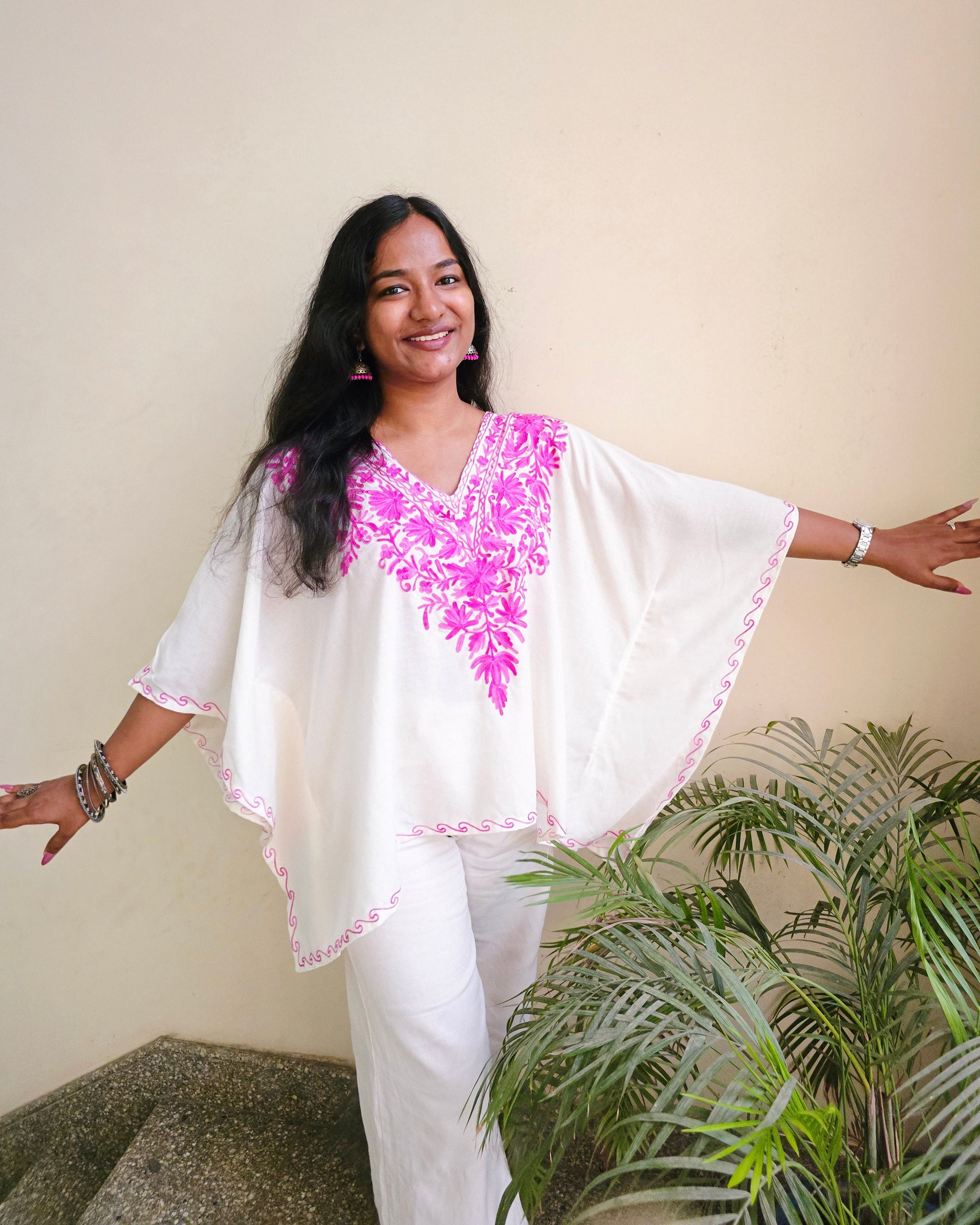 Woman in a white and pink traditional outfit standing indoors with a plant in the background