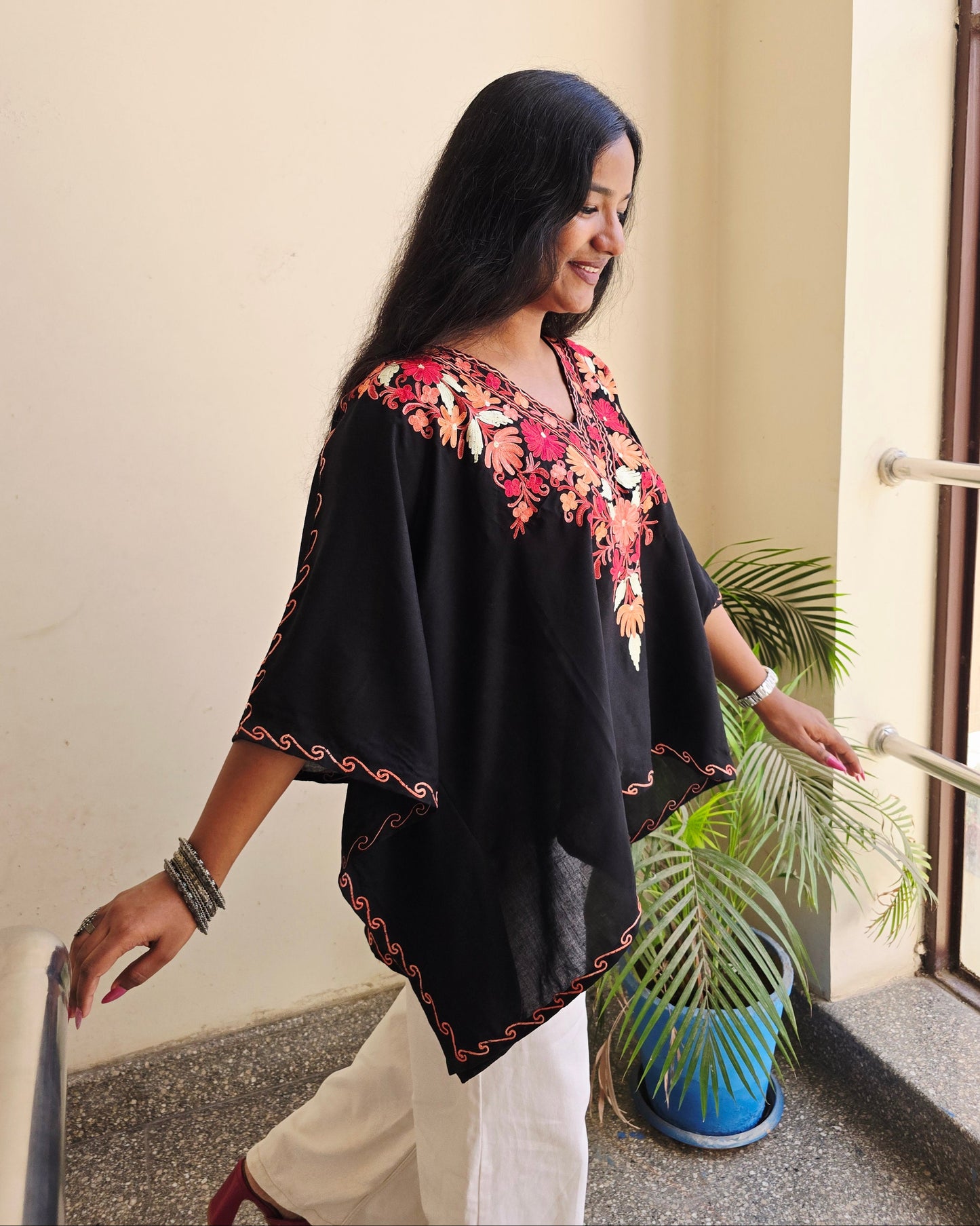 Woman in a black and floral dress standing indoors with a plant in the background