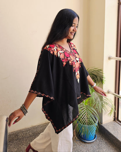Woman in a black and floral dress standing indoors with a plant in the background