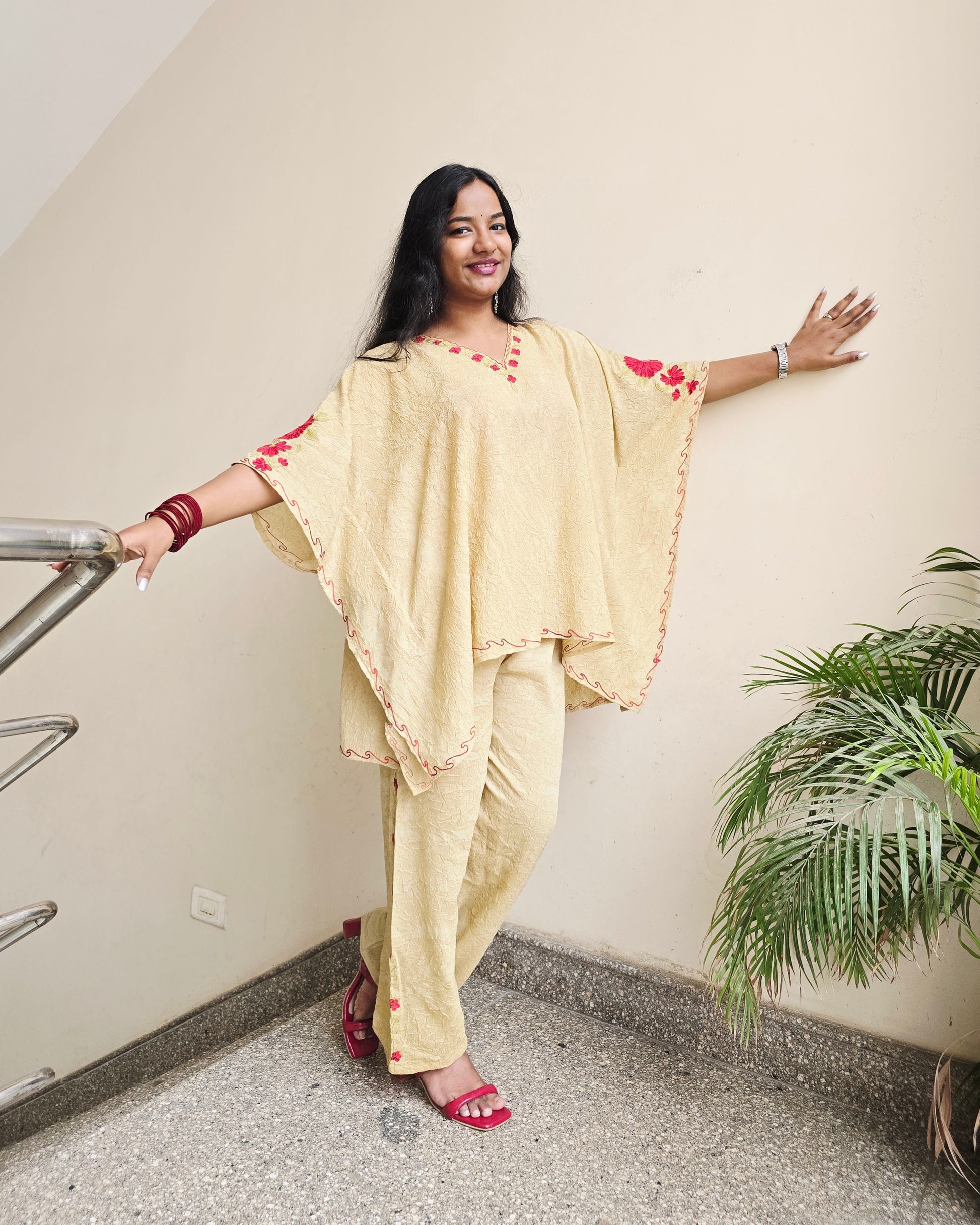 Woman in a yellow saree standing on a ladder indoors with a plant in the background