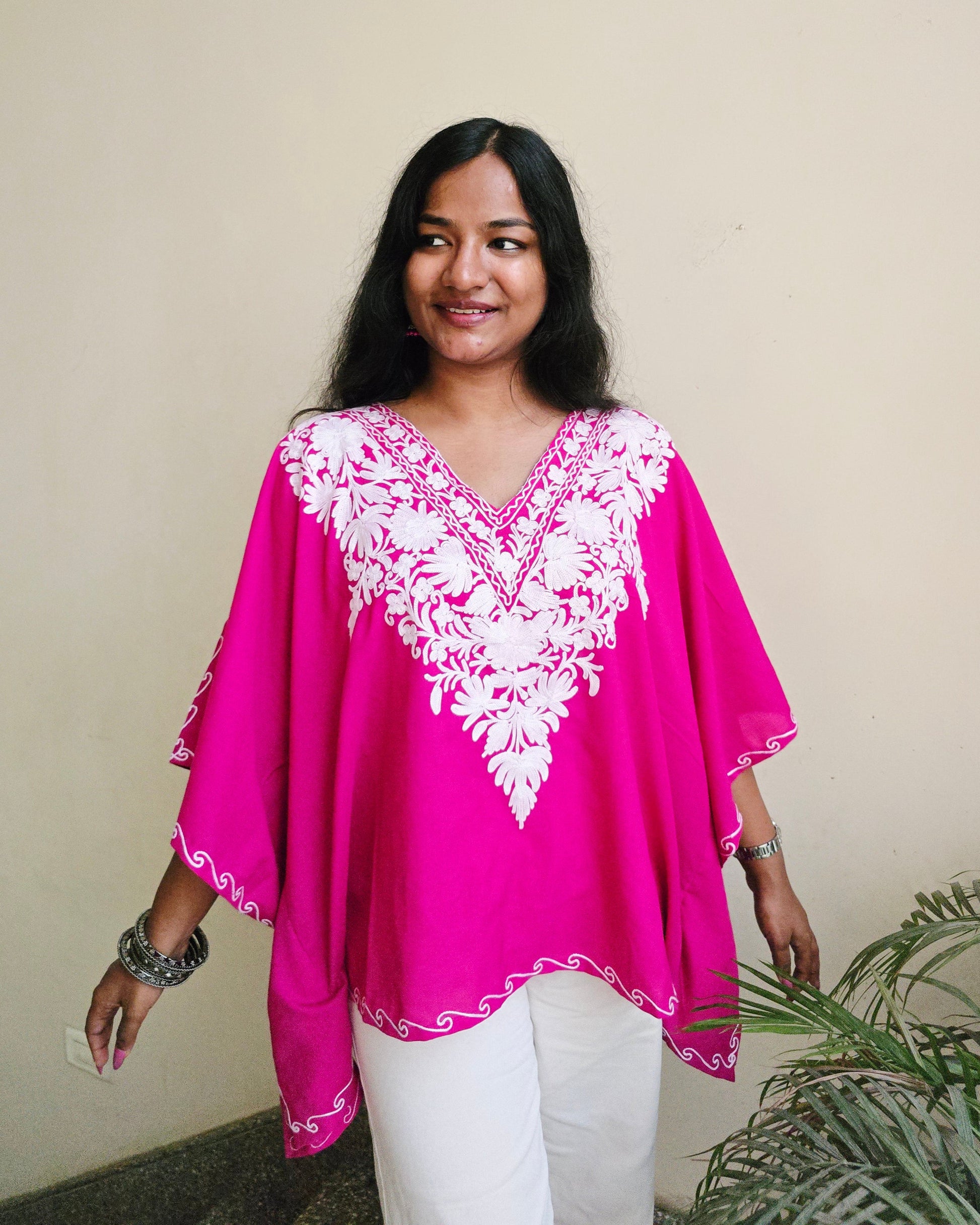 Woman wearing a bright pink top with white floral embroidery indoors.