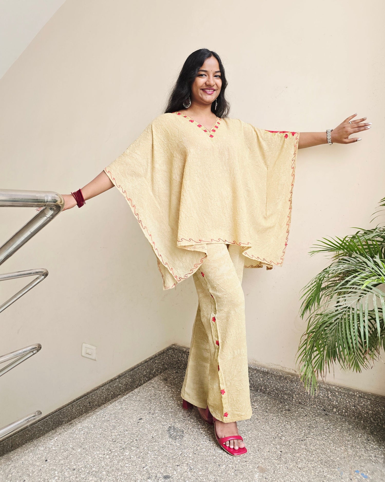 Woman in a light yellow traditional outfit standing on a staircase with a plant in the background.