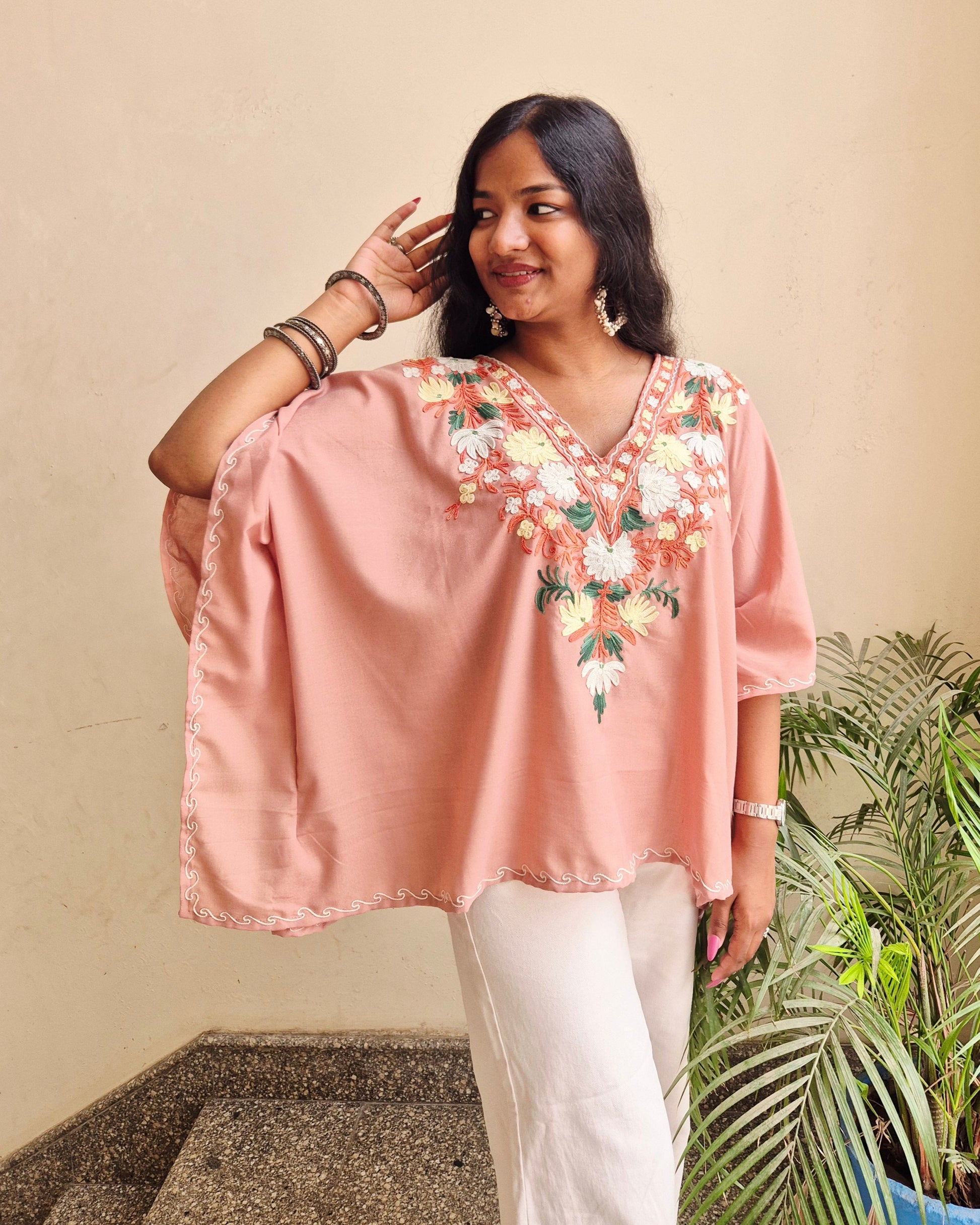 Woman wearing a pink embroidered top with a neutral background