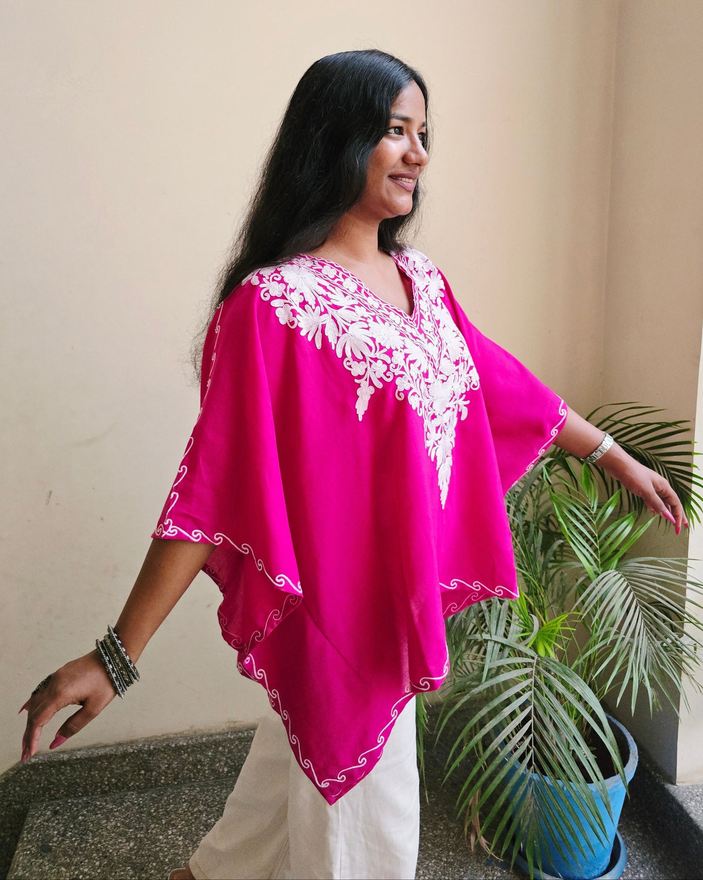 Woman in a bright pink traditional outfit with white patterns, standing indoors.