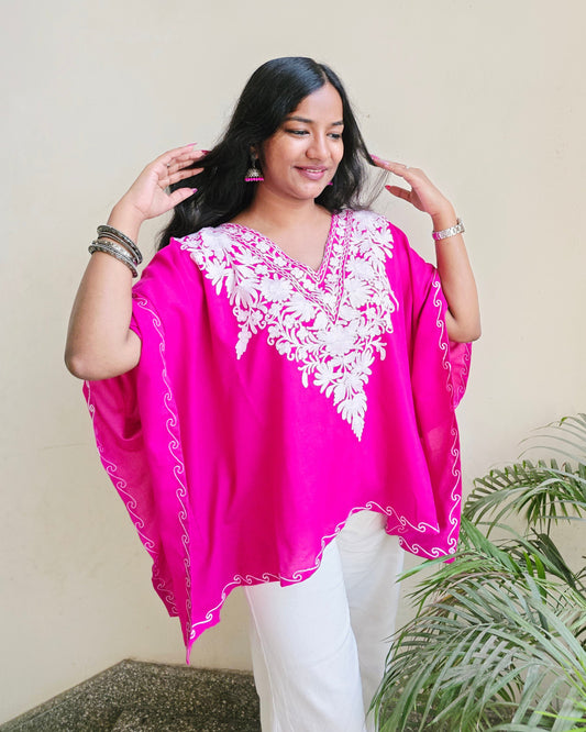 Woman wearing a pink blouse with white embroidery in an indoor setting
