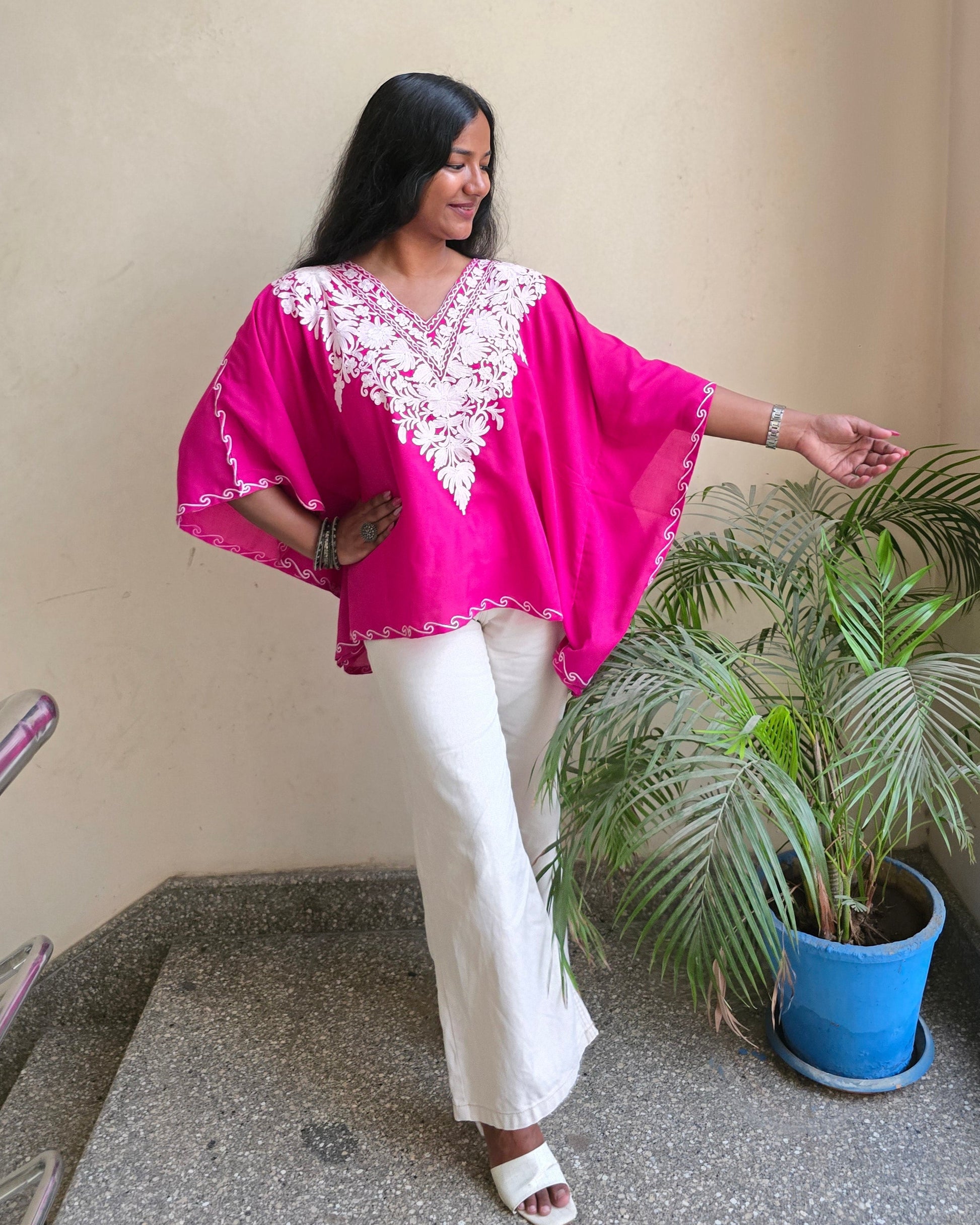 Person wearing a bright pink top with white patterns and white pants, standing indoors.