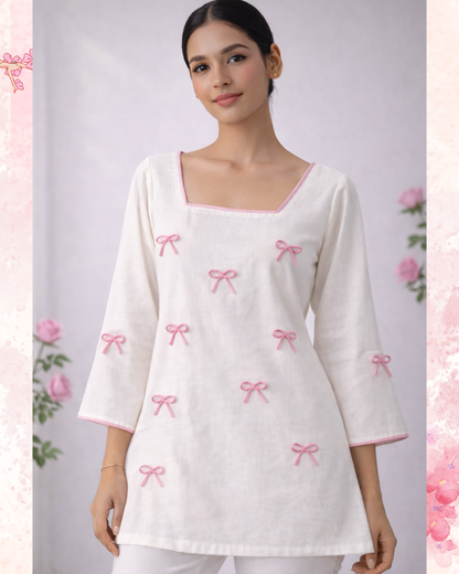 Woman wearing a white top with pink bow patterns on a light gray background