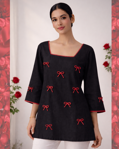 Woman wearing a black top with red bow patterns against a floral background